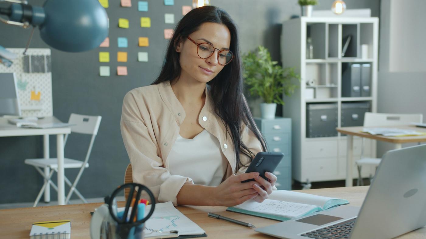 A small-business owner at her desk checking a message on her smartphone